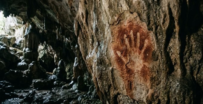 Detalhe de uma arte rupestre mais antiga do mundo, uma estêncil de mão pré-histórica de 67.800 anos com formato de garra, gravada em uma parede de caverna de ca
