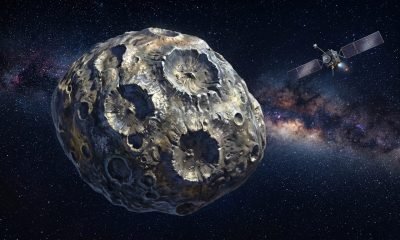 Ilustração artística do Asteroide 16 Psyche, um corpo metálico com crateras de impacto, flutuando no espaço enquanto a missão Psyche da NASA se aproxima.