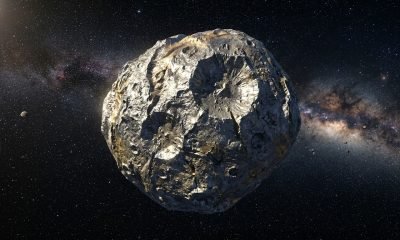 Ilustração artística do asteroide Psyche, um corpo metálico no cinturão principal, com crateras visíveis, representando seu potencial como núcleo de um planeta perdido.