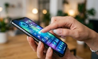 Mão com unhas longas e esmalte condutor transparente interagindo facilmente com a tela sensível ao toque de um smartphone, demonstrando a inovação da tecnologia