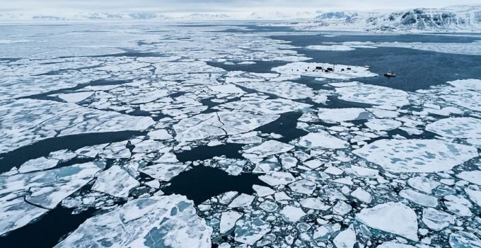 Vista aérea do gelo marinho Ártico em seu recorde mínimo de extensão no inverno, com grandes blocos de gelo fino e água escura visíveis, ilustrando o impacto da