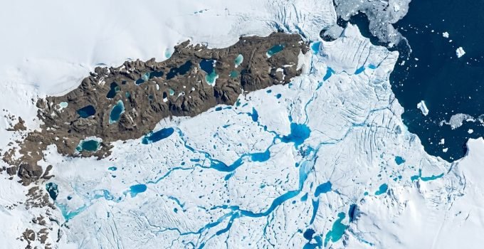 Vista aérea dos lagos de degelo azuis na Antártida, com canais de água derretida sobre a plataforma de gelo Nivlisen, um sinal do aquecimento global.