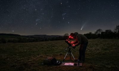 Um astrônomo amador se preparando para a observação do céu em abril de 2026, com um telescópio em um campo escuro sob um céu estrelado, onde um cometa brilha.