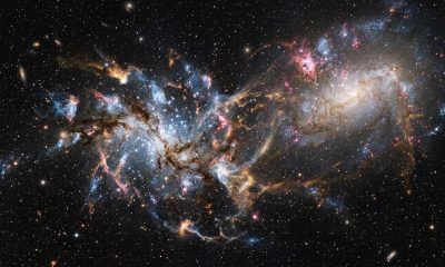 A representação artística da Pequena Nuvem de Magalhães em caos após uma colisão galáctica, com estrelas dispersas e um fundo cósmico estrelado, mostrando a Grande Nuvem de Magalhã