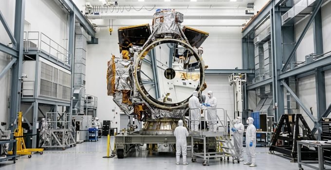 O Telescópio Espacial Nancy Grace Roman, completo e imponente, é visto dentro de uma sala limpa da NASA, com técnicos ao fundo, pronto para futuras descobertas.