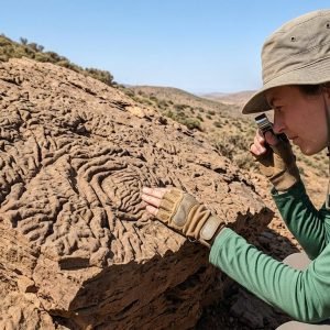 Geóloga Rowan Martindale examinando rocha com textura de pele de elefante em Marrocos, evidenciando fósseis de vida antiga em oceanos profundos.